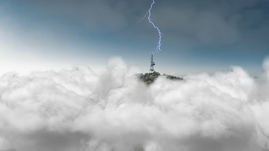 Thunder strike on satellite tower on top of a mountain surrounded by clouds.