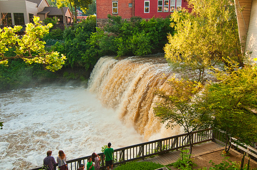 Chagrin Falls, OH, USA - June 28, 2015: As exemplified by the family and young couple in this scene, the viewing platform next to the falls is a popular gathering spot to see the water roar over the brink after heavy rains.