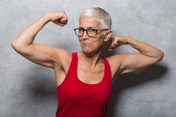 Woman making a grimace while showing muscles Mature woman showing biceps and making funny face bicep photos stock pictures, royalty-free photos & images
