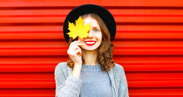 istock Happy cool girl  hides one eye yellow maple leaf on a red background 1013795892
