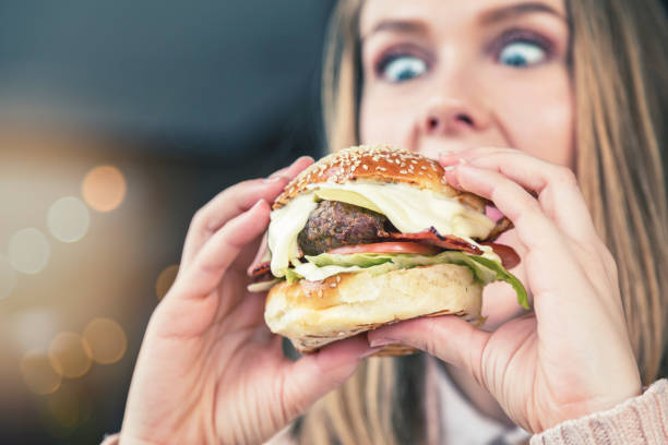 Ragazza dagli occhi spalancati guarda dall'alto in basso l'enorme hamburger - foto stock