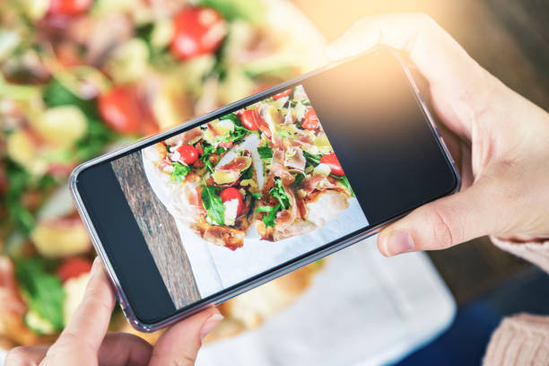 istock Hands using phone to photograph pizza at restaurant 1013813238