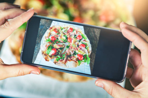 istock Hands using phone to photograph pizza at restaurant 1013813240