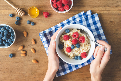 Eating healthy breakfast. Oatmeal porridge with raspberries, blueberries in hands. Girl eating oats for breakfast. Top view, selective focus