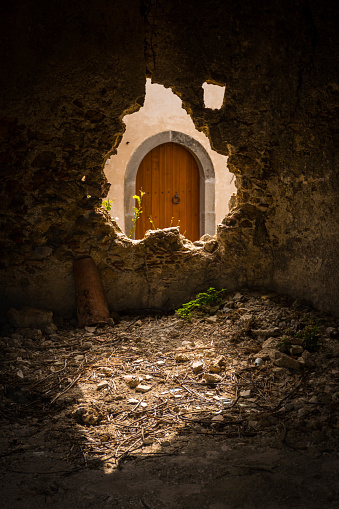 An old wooden arched door in Sicily seen through a broken hole in a stone wall