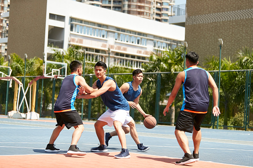 group of young asian adult players playing basketball on outdoor court.