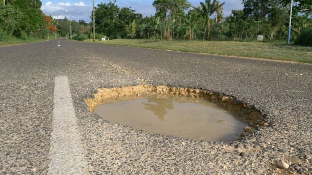 primo: il sole tropicale splende su una grande buca nel mezzo della strada in decomposizione. - middle of the road immagine foto e immagini stock