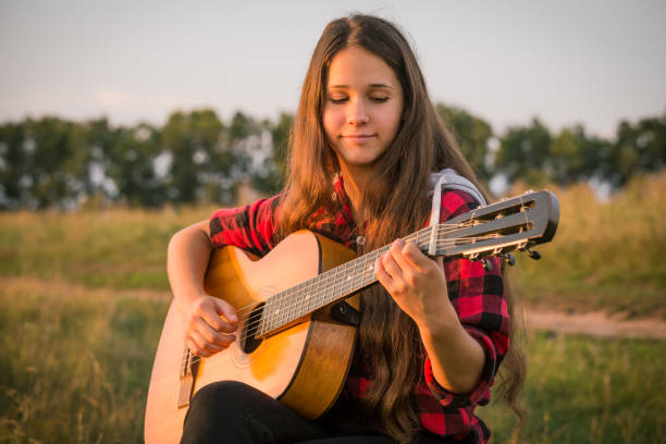 Young girl playing the guitar on meadow at sunset, outdoors