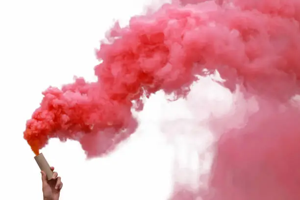 Human hand holding smoke bombs with red smoke, isolated on white background.
