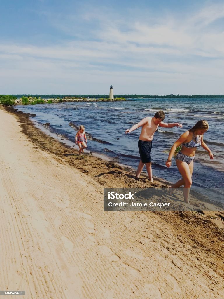 Line of play on Lake Michigan Three children walking on the shoreline of Lake Michigan in Gladstone, Michigan with a Lighthouse in the background Michigan Stock Photo