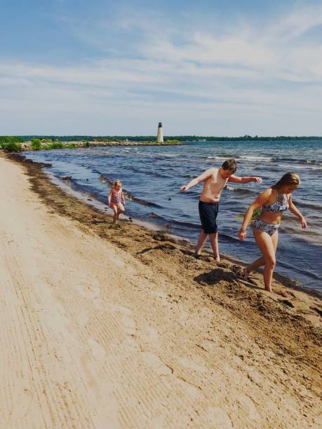 Line of play on Lake Michigan Three children walking on the shoreline of Lake Michigan in Gladstone, Michigan with a Lighthouse in the background gladstone michigan stock pictures, royalty-free photos & images