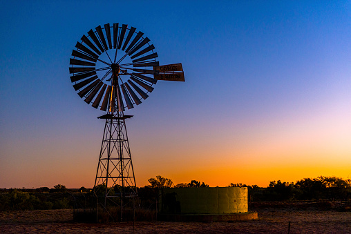 A windmill is silhouetted against a blue sky at sunset.