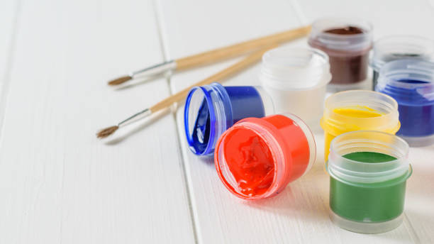 istock Several overturned jars of gouache and a brush on a white wooden table. Creative kit. 1013979402