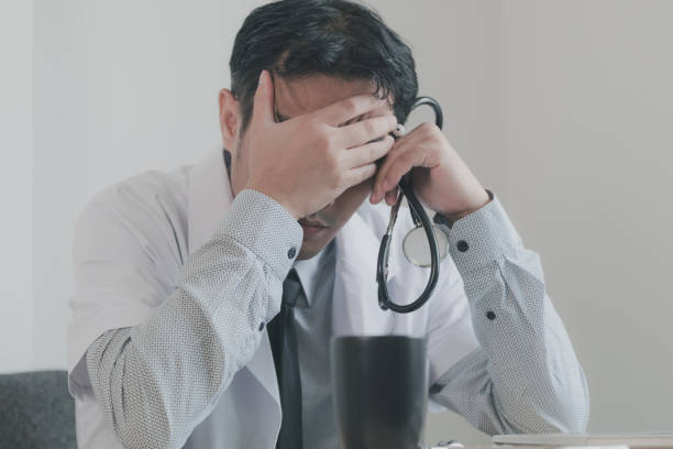 istock Asian young man doctor in white uniform has stress form hard work while sitting on his desk 1013999412