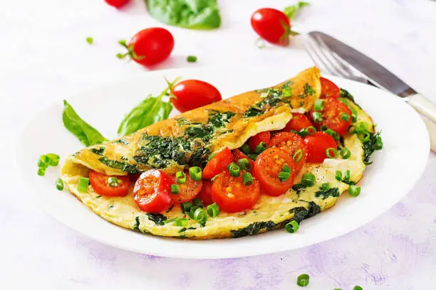 Omelette with tomatoes, spinach and green onion on white plate.  Frittata - italian omelet.