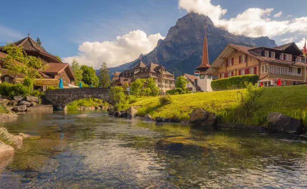 The traditional town of Kandersteg in the Lotschental valley of the Swiss alps, with a river running beside a church and river with mountains in the background.