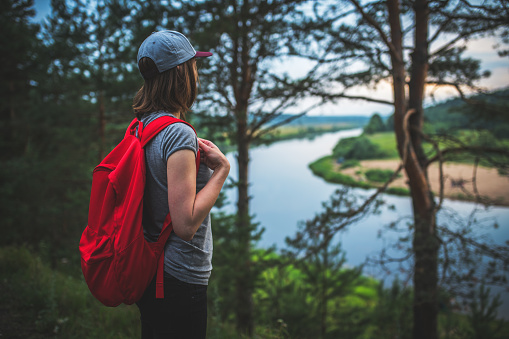 Young woman traveler with red backpack in the woods