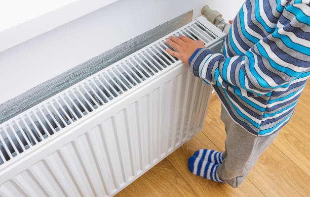 Heating radiator at home. A child in woolen sweater warms his hands near the heater. Heating radiator at home. A child in woolen sweater warms his hands near the heater. warms stock pictures, royalty-free photos & images