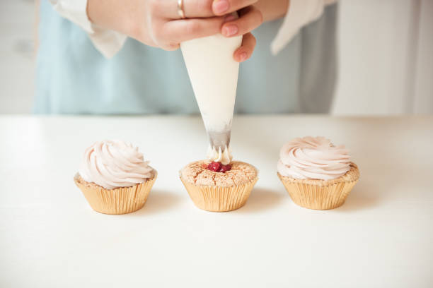 istock Close up hands of the chef with confectionery bag squeezing cream on cupcakes 1014047708