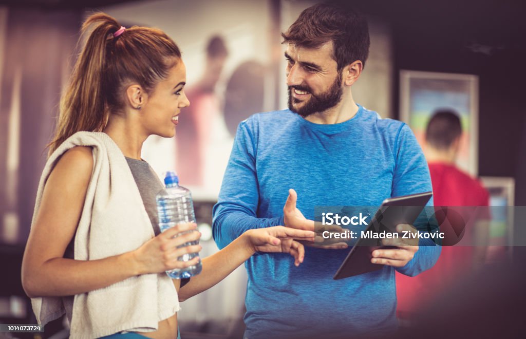 Advise for exercise. Coach talking with sports girl at gym. Fitness Instructor Stock Photo
