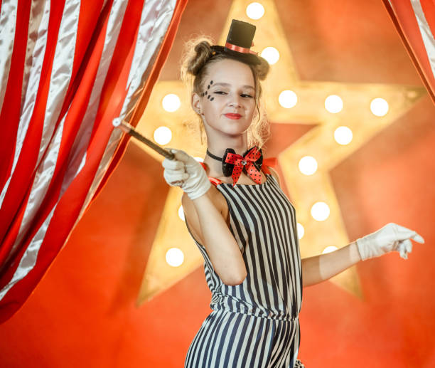 istock Cheerful Young Girl Illusionist Points with Magic Wand on Something 1014078162