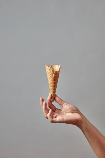 A woman's hand holds an empty waffle cone on a gray background