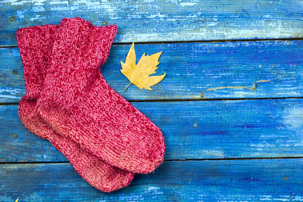 top view rted knitted socks, autumn yellow leaves on blue wooden boards