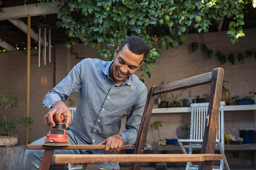 Smiling young man sanding a chair outdoors