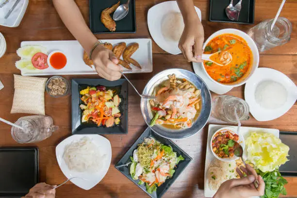 Photo of Top view of friends or family eating Thai food together on wood table.