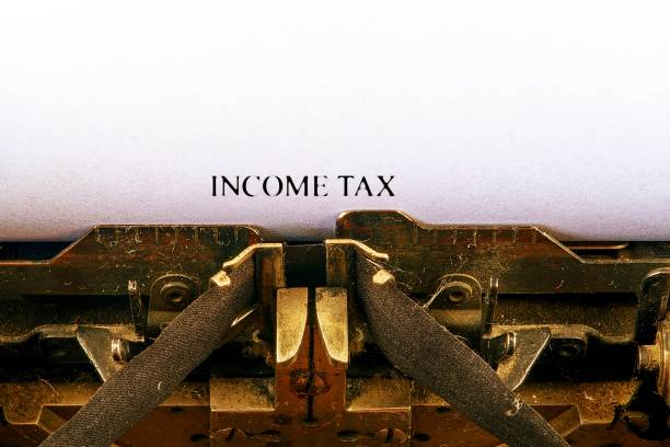 istock Closeup on vintage typewriter. Front focus on letters making INCOME TAX text. Business concept image with retro office tool 1014108398