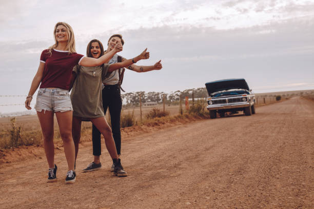 donne in autostop vicino alla loro auto rotta su strada di campagna - vehicle breakdown car stranded women foto e immagini stock