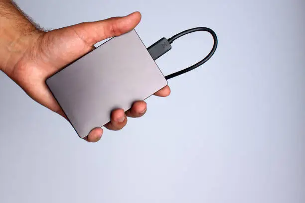 A man's hand holds a portable hard drive on a gray background