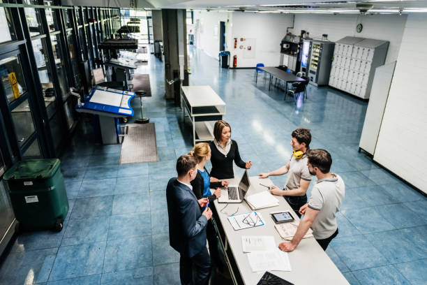Meeting Between Engineers On Factory Floor A meeting between a group of engineers at a table on a printing factory floor. digital printing house stock pictures, royalty-free photos & images