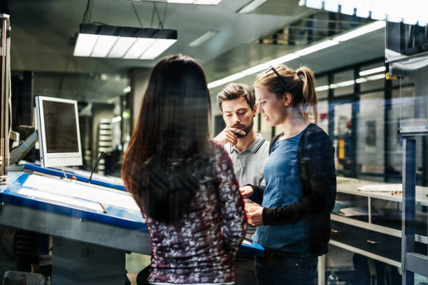 Printing Plant Engineers Working Together At Console A group of printing plant engineers talking and working together at a large console. printing plant stock pictures, royalty-free photos & images