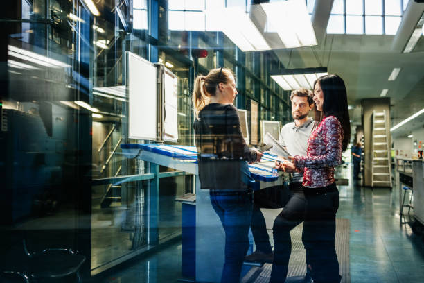 Team Of Engineers Having Discussion At Desk A team of engineers having a discussion at a desk in a large printing factory. digital printing house stock pictures, royalty-free photos & images