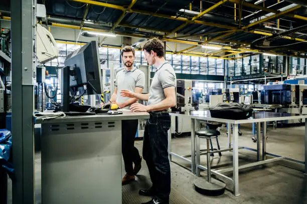 Two printing factory engineers working at a console together.