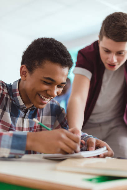 istock Smiling african american schoolboy writing in textbook and classmate standing behind 1014158566