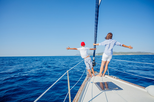 Back view of Boy with his mother on board of sailing yacht on summer cruise. Travel adventure, yachting with child on family vacation.
