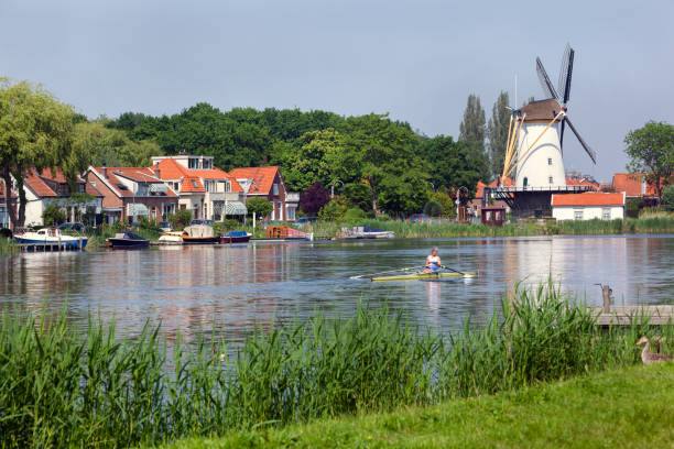 The idyllic river Rotte in Rotterdam with an old white windmill and some houses at the other side while a rowing boat is passing by