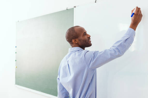 istock Smiling african american teacher writing on white board in classroom 1014160194