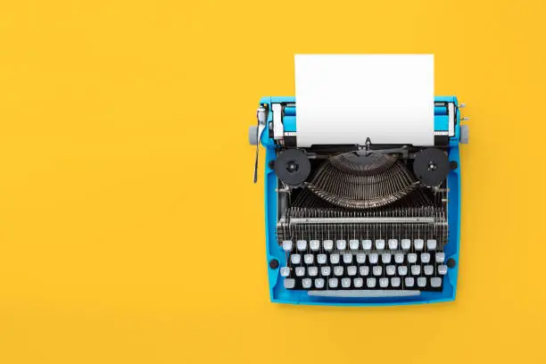 Photo of Typewriter machine in retro style on yellow background.