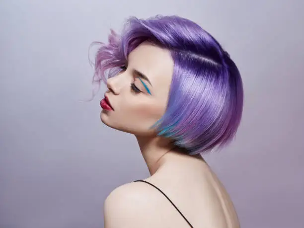 Photo of Portrait of a woman with bright colored flying hair, all shades of purple. Hair coloring, beautiful lips and makeup. Hair fluttering in the wind. Sexy girl with short  hair. Professional coloring