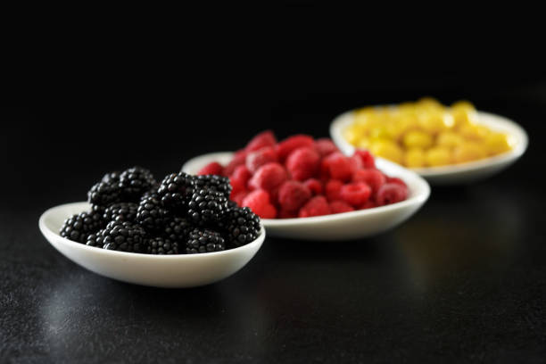 juicy raspberry, blackberries and dogeberry in white plate on black background