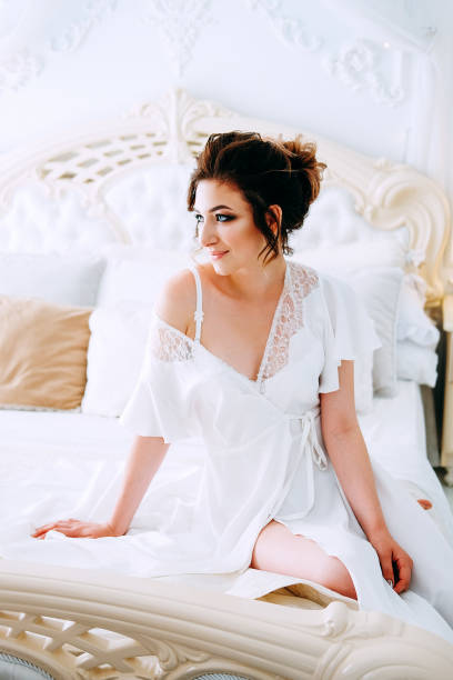 istock Sensual brunette in silk white robe waiting on the bed looking calm and relaxed 1014174348