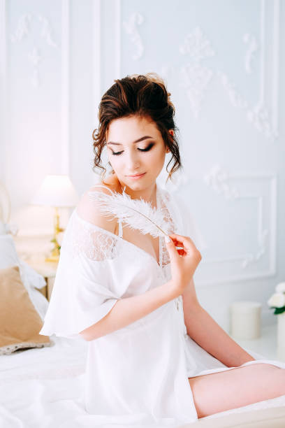 istock Sensual brunette in silk white robe waiting on the bed looking calm and relaxed 1014174376
