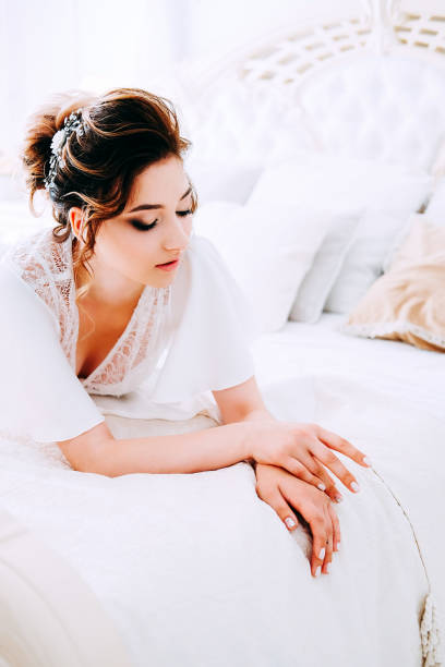 istock Sensual brunette in silk white robe waiting on the bed looking calm and relaxed 1014174526