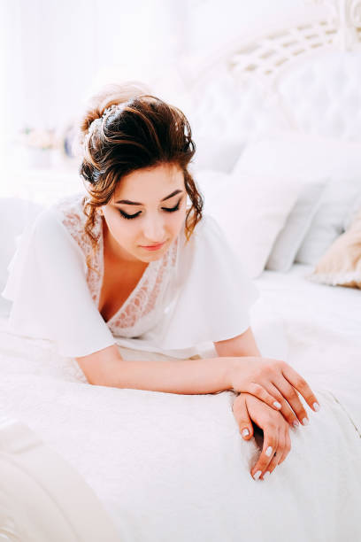istock Sensual brunette in silk white robe waiting on the bed looking calm and relaxed 1014174528