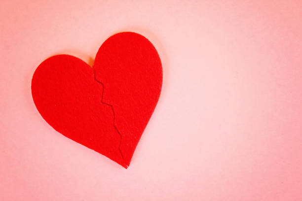 istock Red felt heart broken into two halves on a pink background. 1014179448