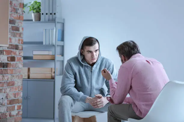 Photo of A psychology specialist explaining an action plan for recovery to a troubled teenage boy during an individual therapy session.