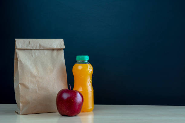 коричневый бумажный мешок и красное яблоко на фоне доски. - lunch bag apple brown стоковые фото и изображения